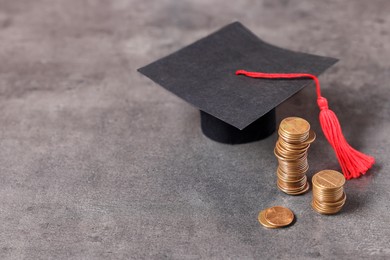 Photo of Graduate hat and coins on grey textured table, space for text. Tuition payment