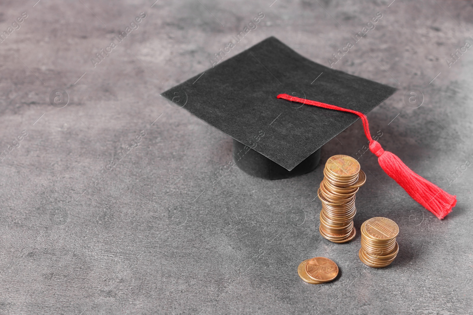 Photo of Graduate hat and coins on grey textured table, space for text. Tuition payment