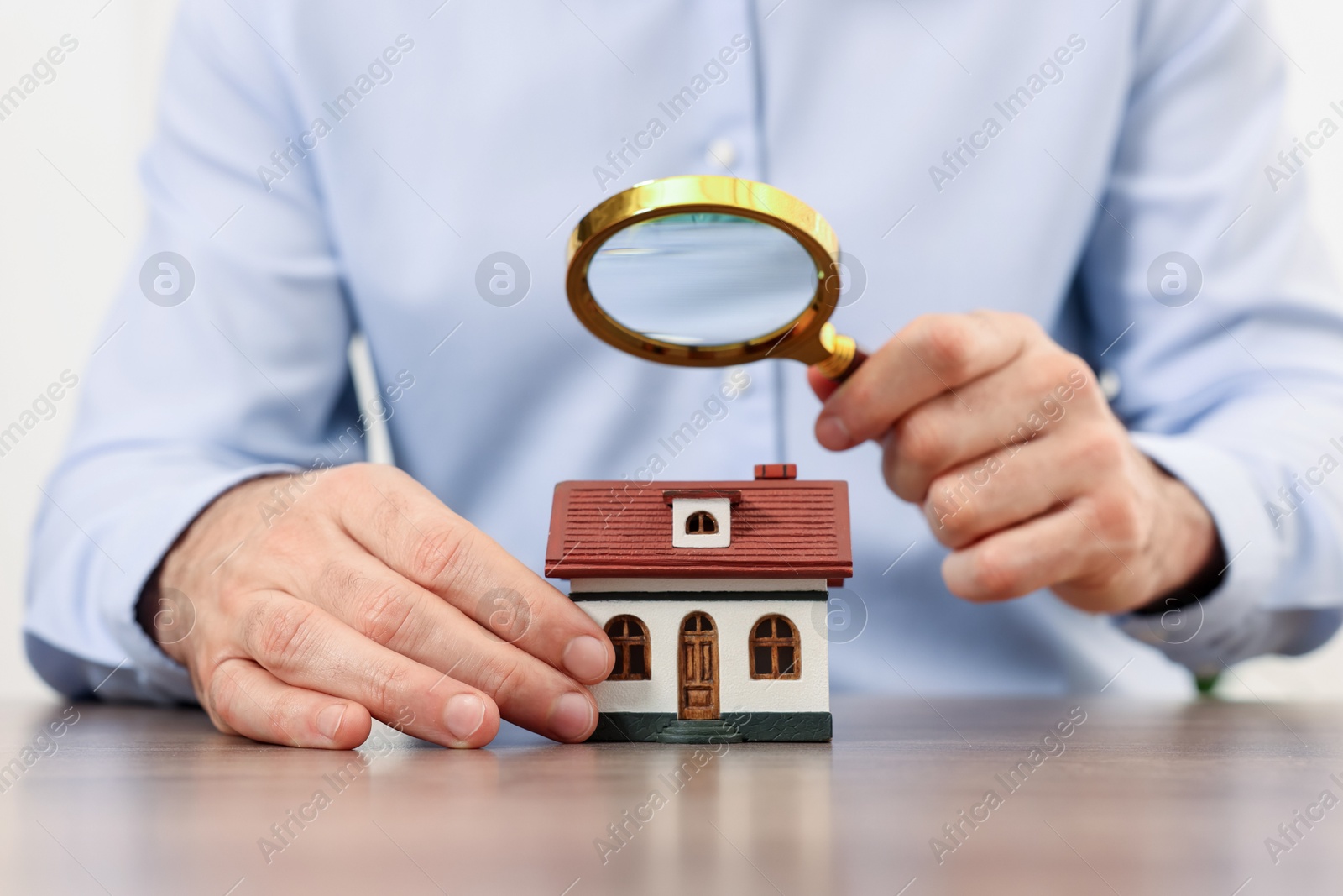 Photo of Real estate agent looking at house figure through magnifying glass at wooden table in office, closeup. Home appraisal