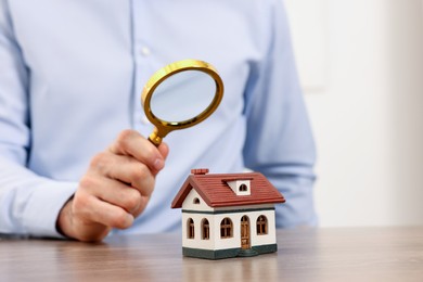 Photo of Real estate agent looking at house figure through magnifying glass at wooden table in office, closeup. Home appraisal