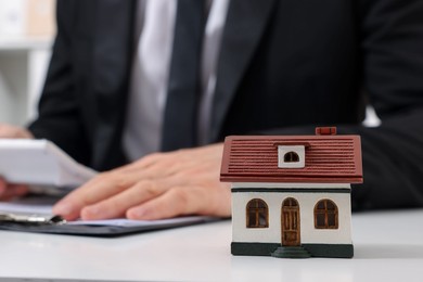 Photo of House figure and real estate agent with calculator at white table in office, selective focus. Home appraisal