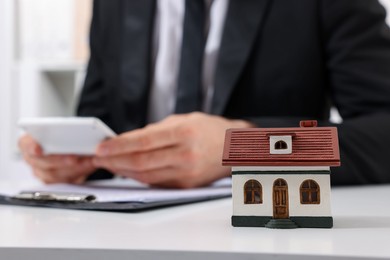 Photo of House figure and real estate agent with calculator at white table in office, selective focus. Home appraisal