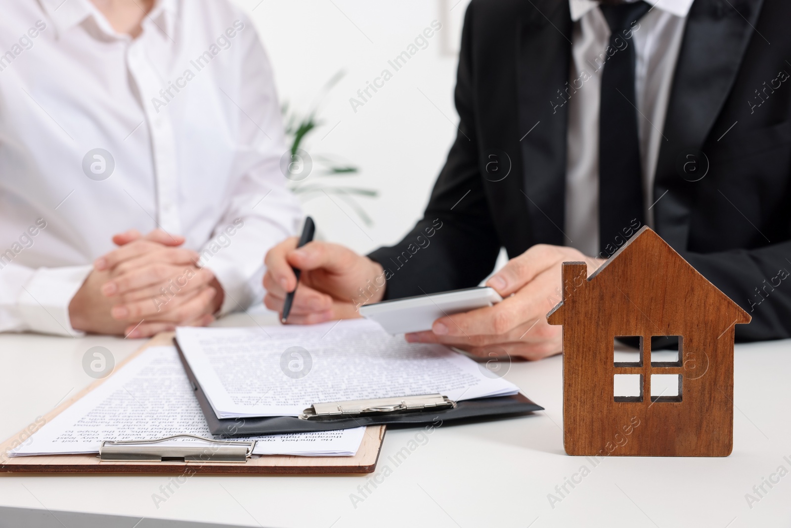 Photo of Real estate agent showing client where to sign document at white table in office, focus on house figure. Home appraisal