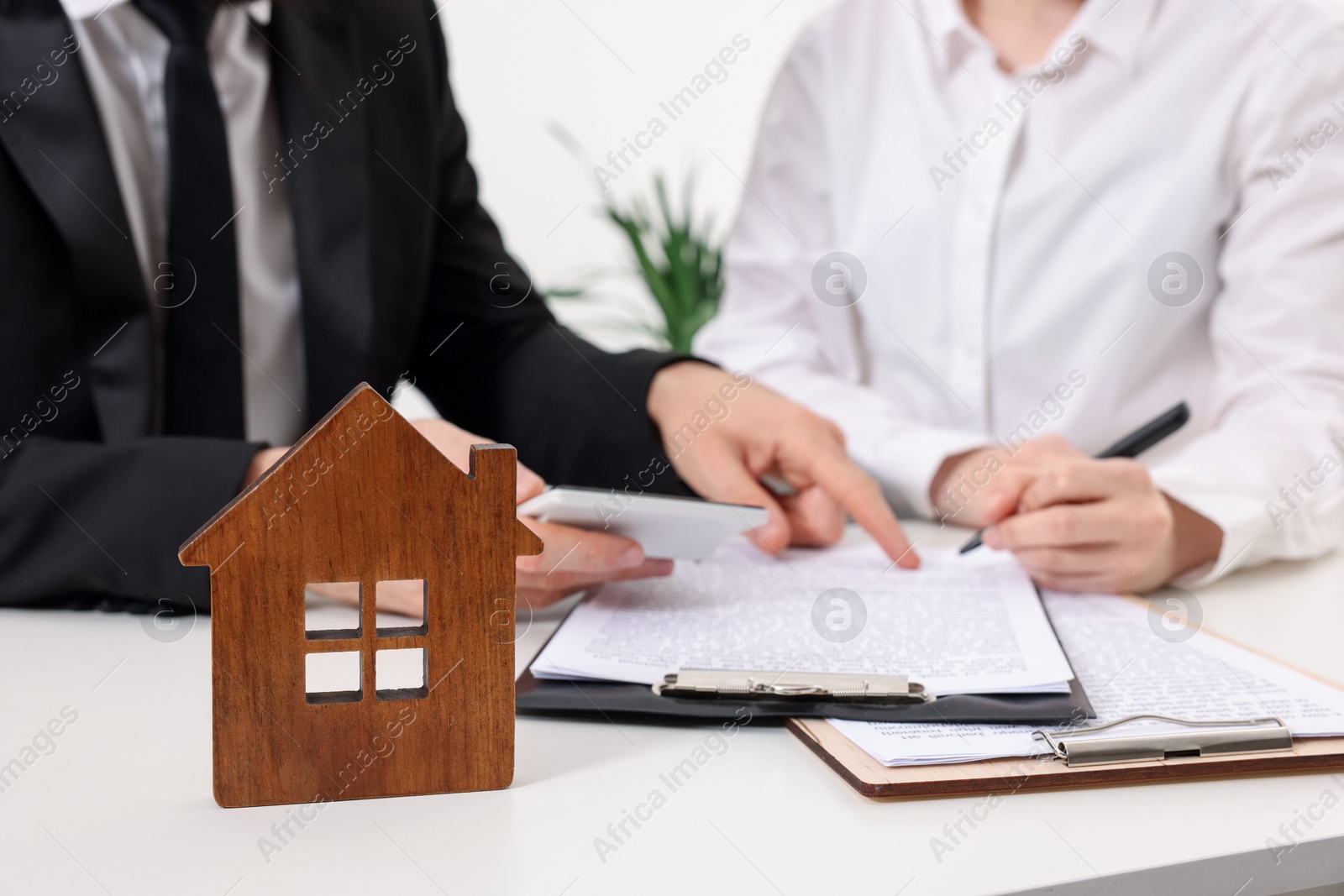 Photo of Real estate agent showing client where to sign document at white table in office, focus on house figure. Home appraisal