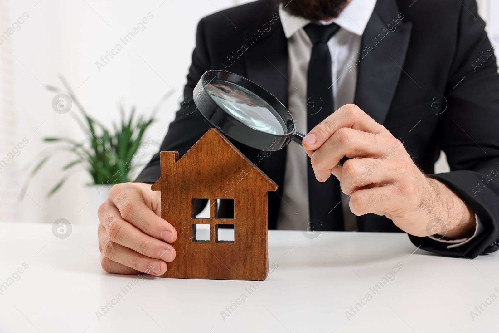 Photo of Real estate agent with house figure and magnifying glass at white table in office, closeup. Home appraisal