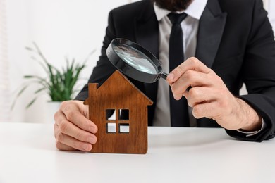 Photo of Real estate agent with house figure and magnifying glass at white table in office, closeup. Home appraisal