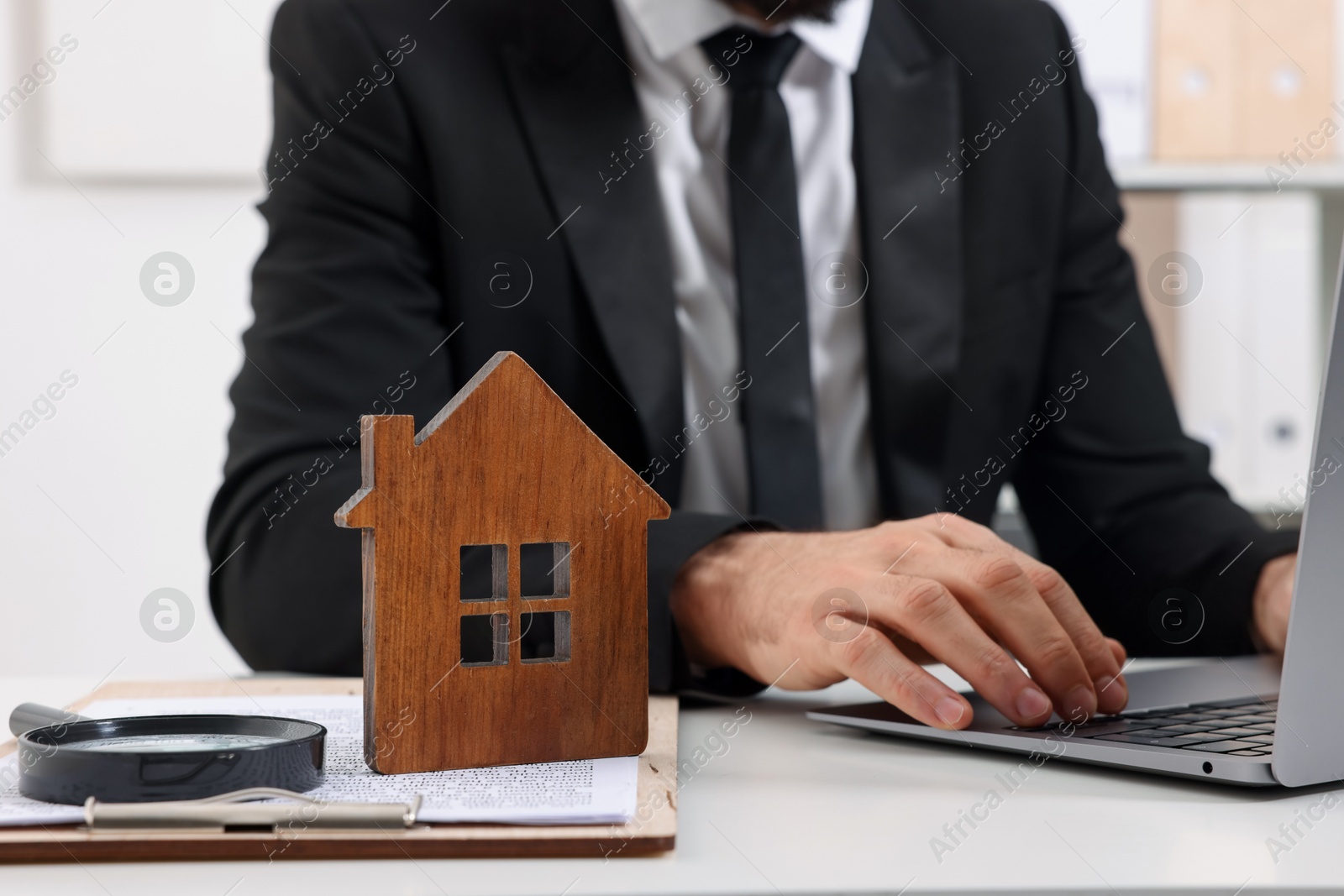 Photo of Real estate agent working with laptop at white table with house figure in office, closeup. Home appraisal