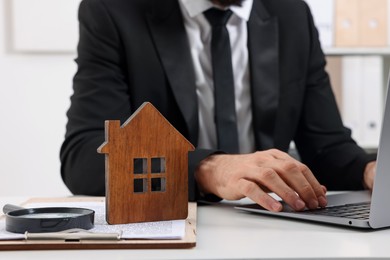 Photo of Real estate agent working with laptop at white table with house figure in office, closeup. Home appraisal