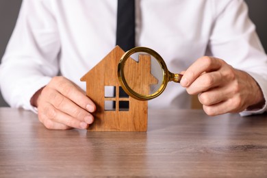 Photo of Real estate agent with house figure and magnifying glass at wooden table, closeup. Home appraisal