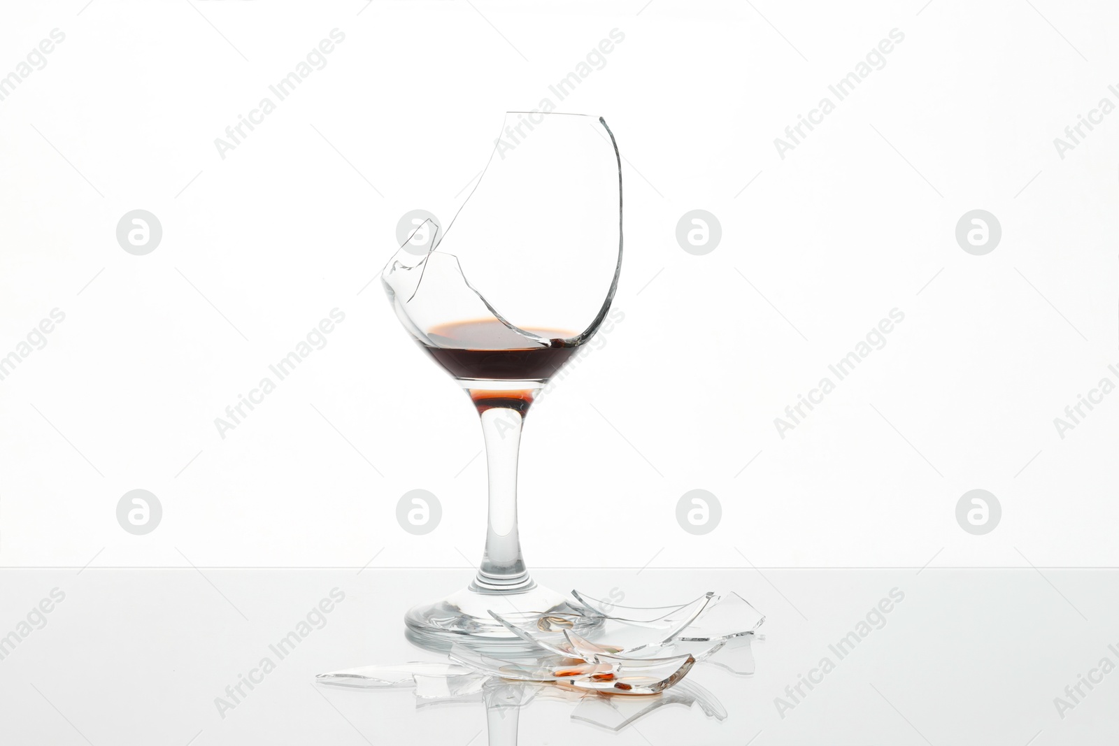 Photo of Pieces of broken glass with wine on table against white background