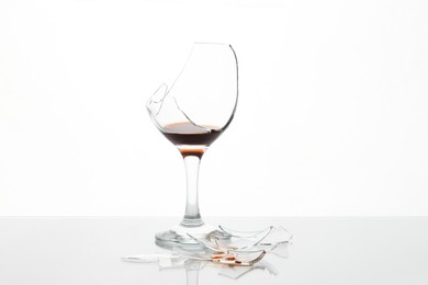 Photo of Pieces of broken glass with wine on table against white background