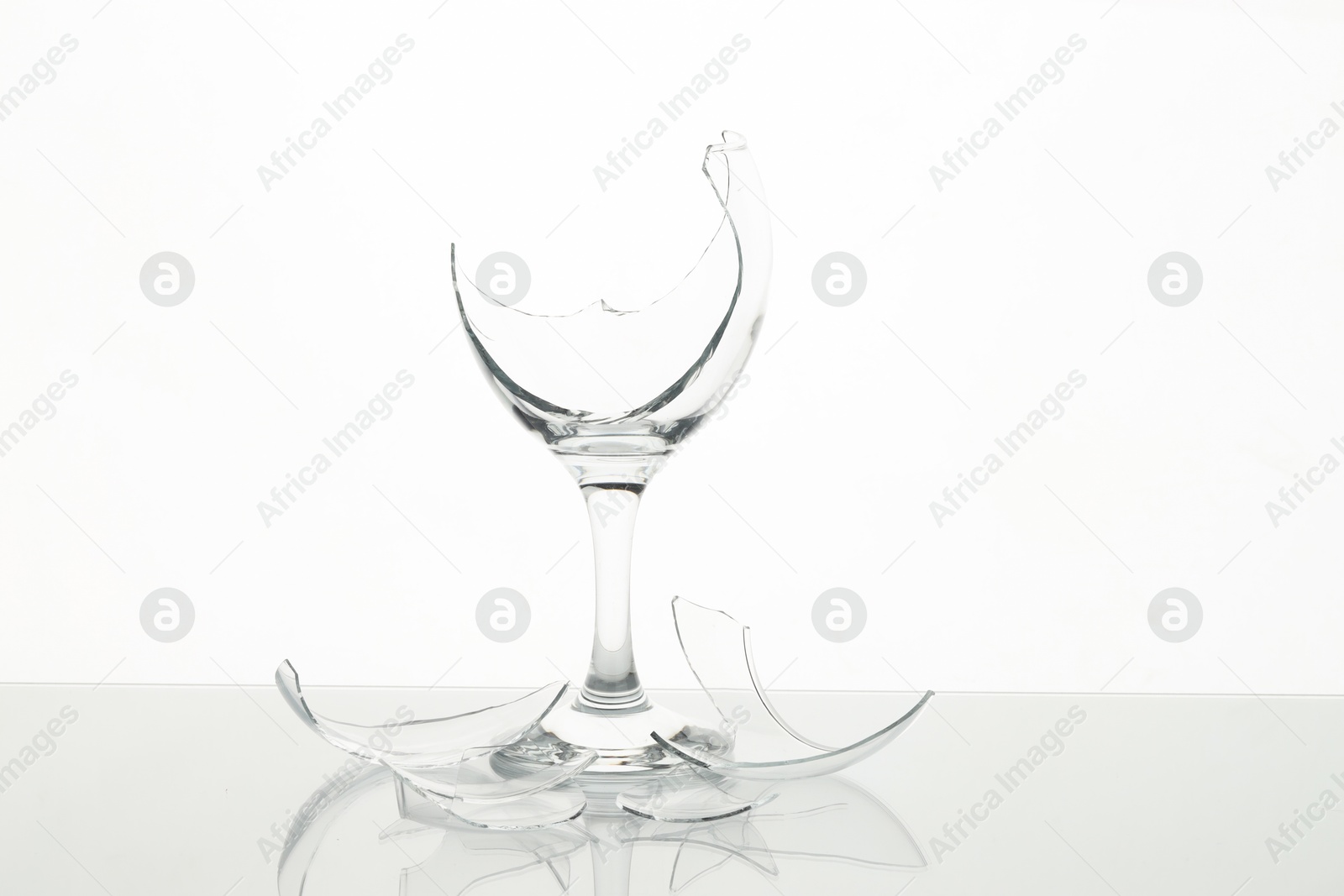 Photo of Pieces of broken wine glass on table against white background