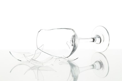 Photo of Pieces of broken wine glass on table against white background, closeup