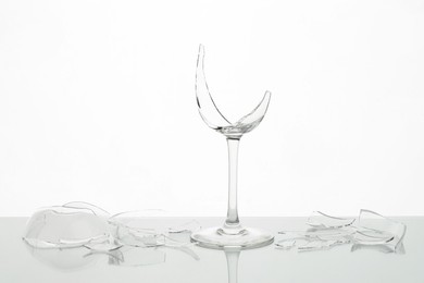 Photo of Pieces of broken wine glass on table against white background