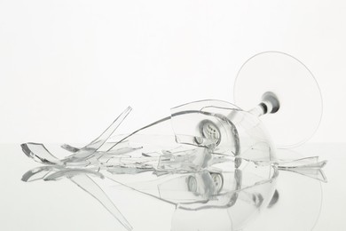 Photo of Pieces of broken wine glass on table against white background, closeup