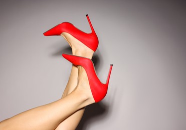 Photo of Woman wearing beautiful red high heeled shoes on light grey background, closeup