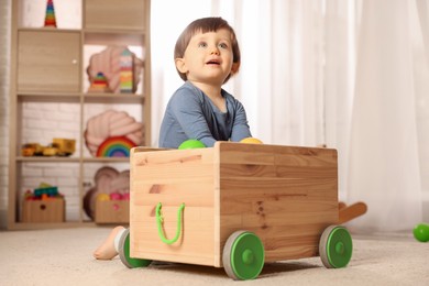 Photo of Cute little boy playing with wooden cart at home