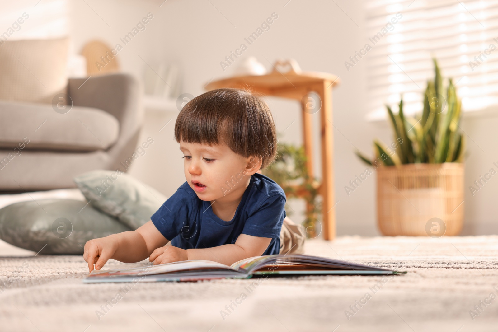 Photo of Cute little boy with book on floor at home