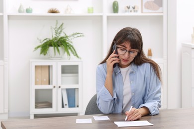 Photo of Paying bills. Woman with different invoices talking on phone at wooden table indoors