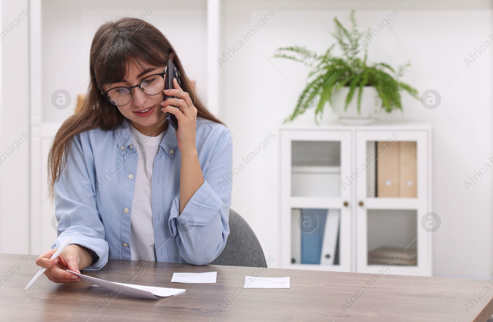 Photo of Paying bills. Woman with different invoices talking on phone at wooden table indoors