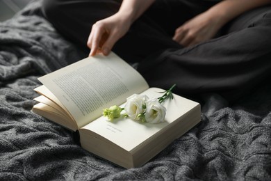 Photo of Woman reading book with beautiful flowers on blanket, closeup