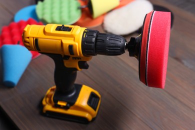 Photo of Electric screwdriver with different polish pads on wooden background, closeup