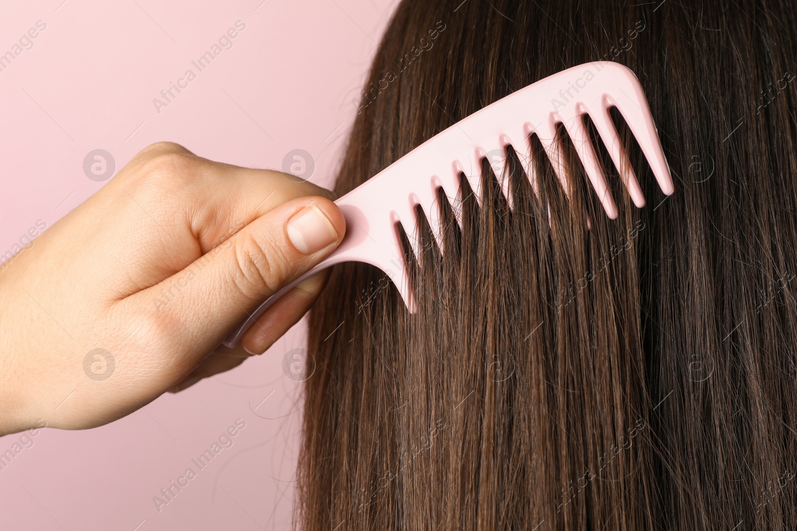 Photo of Woman brushing hair with plastic comb on pink background, closeup