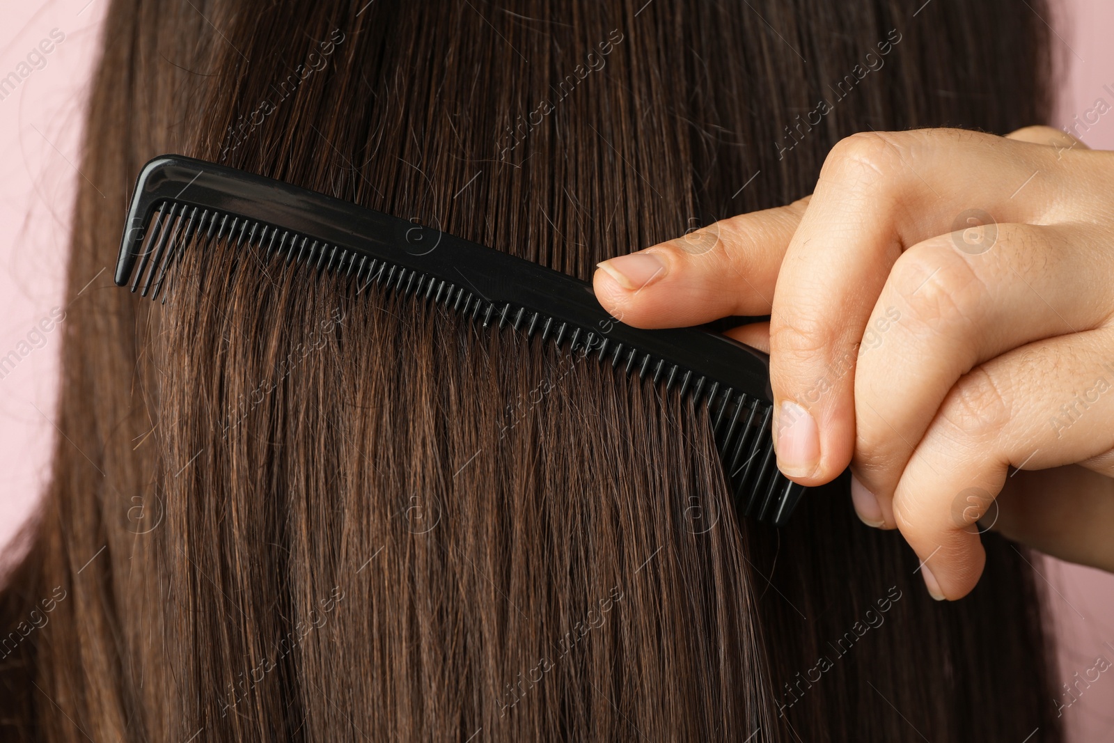 Photo of Woman brushing hair with plastic comb on pink background, closeup