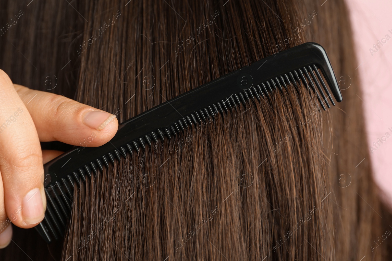 Photo of Woman brushing hair with plastic comb on pink background, closeup