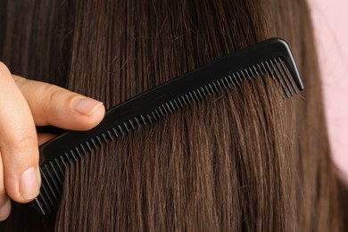 Photo of Woman brushing hair with plastic comb on pink background, closeup