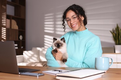 Photo of Beautiful woman with her cute cat working on laptop at desk in home office