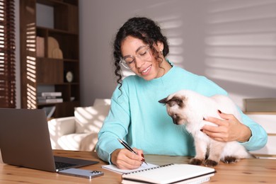 Photo of Beautiful woman with her cute cat working on laptop at desk in home office