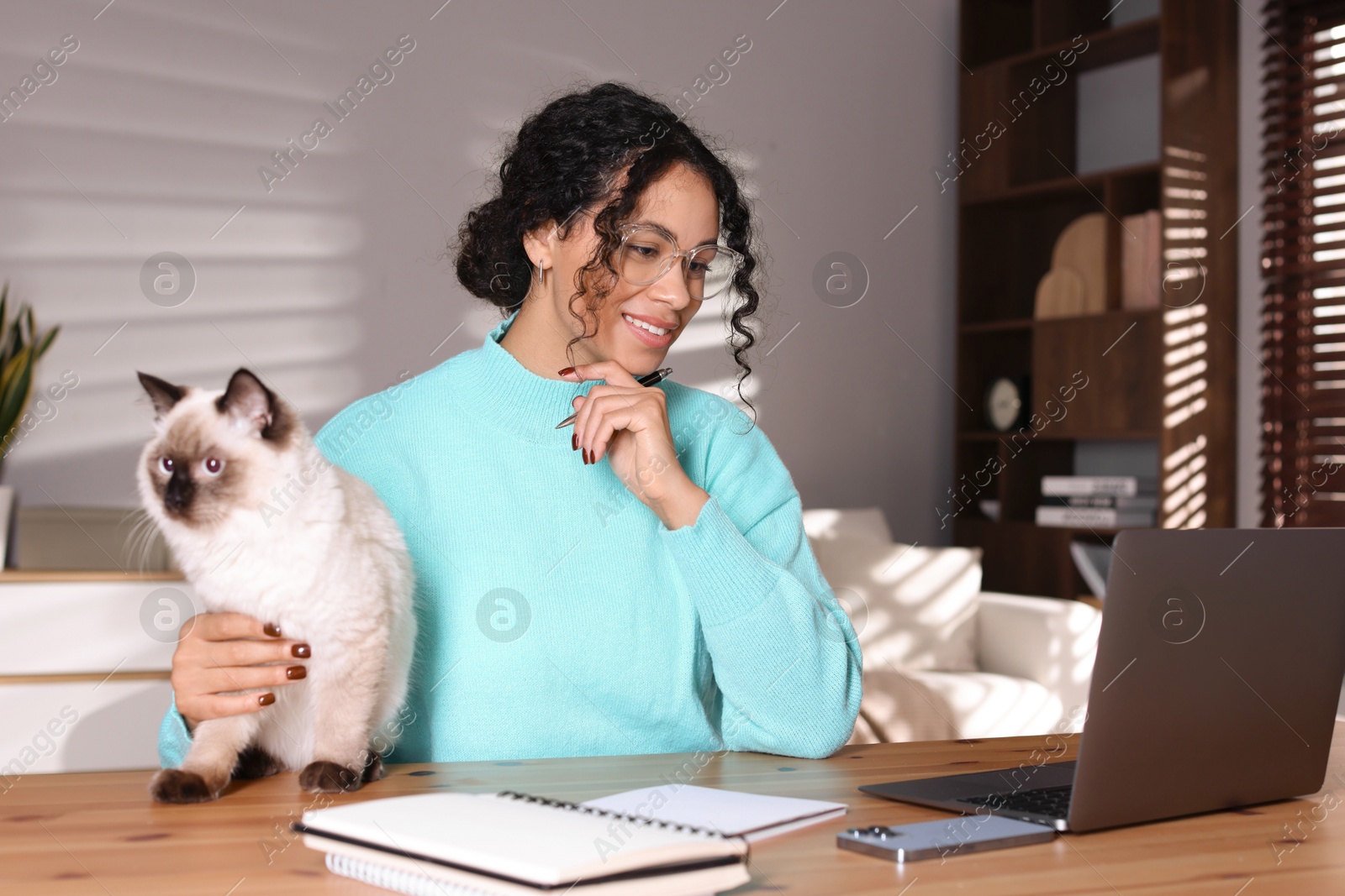 Photo of Beautiful woman with her cute cat working on laptop at desk in home office