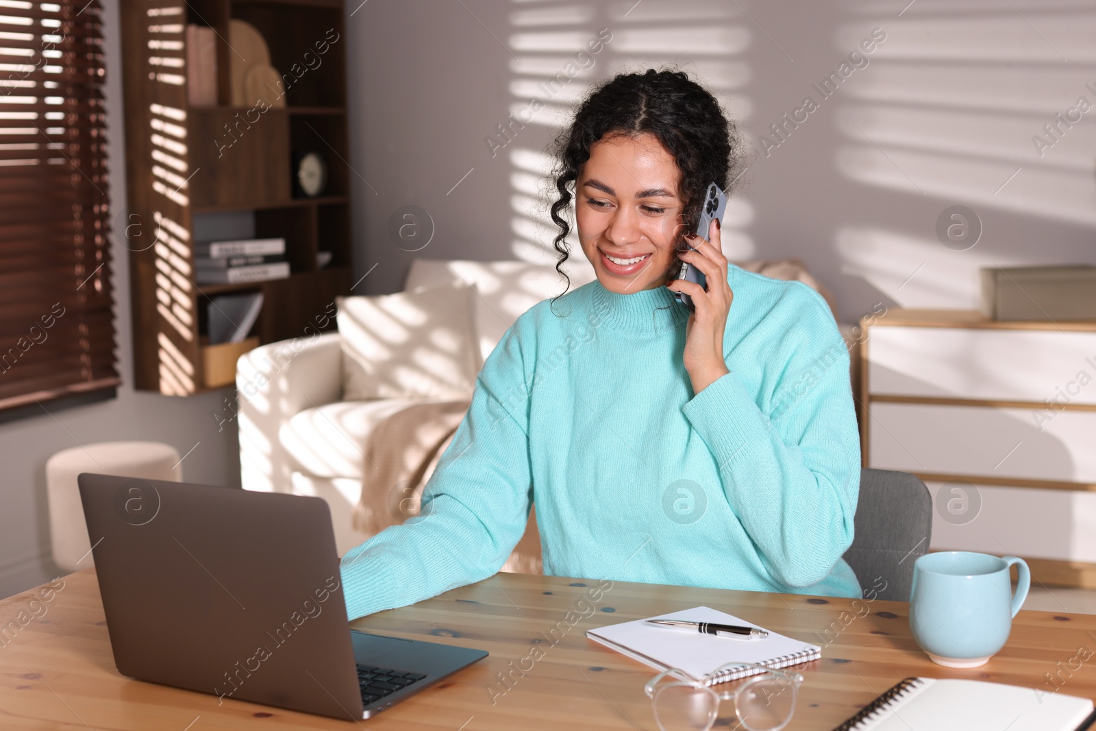 Photo of Beautiful woman talking on phone while working with laptop at desk in home office