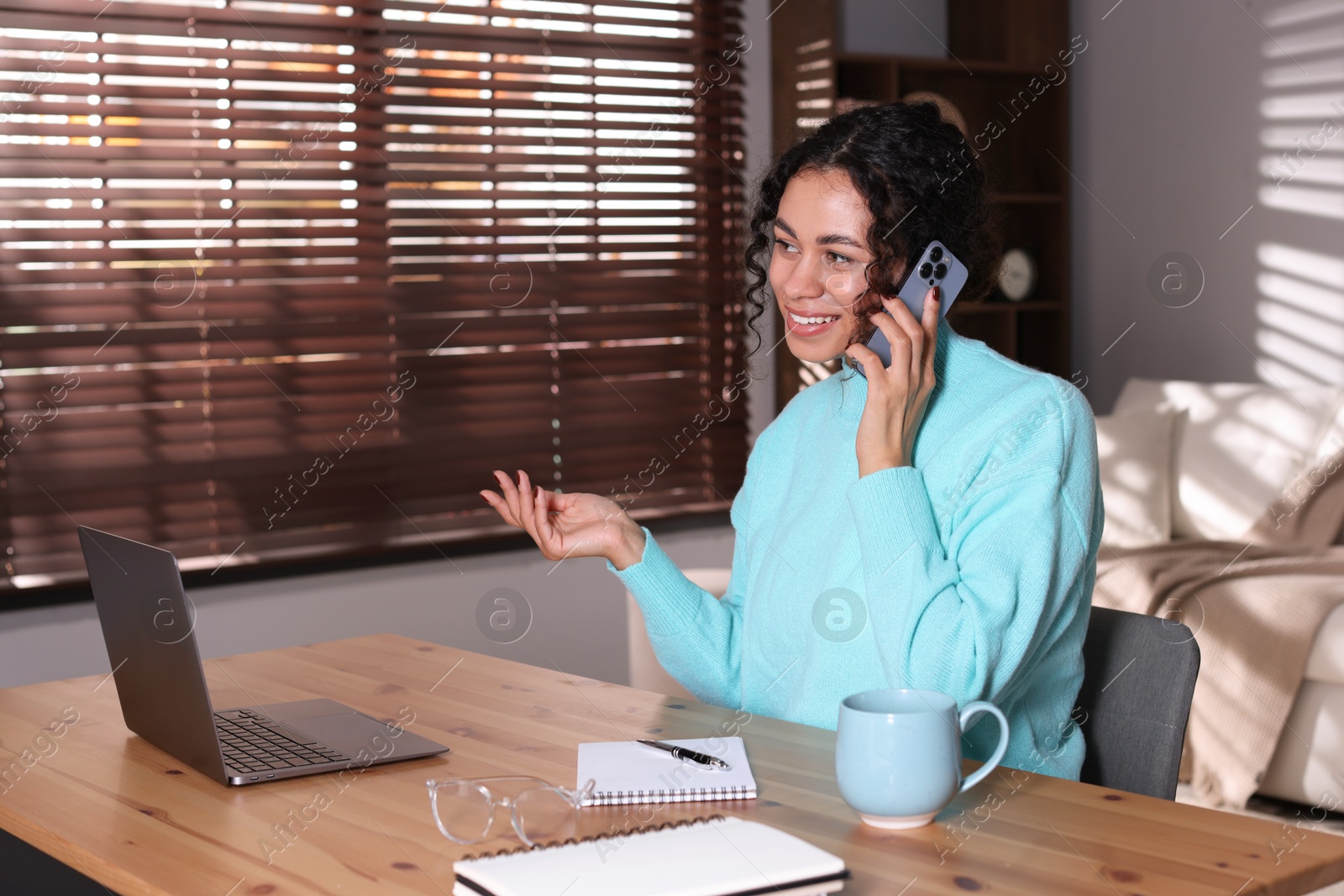 Photo of Beautiful woman talking on phone while working with laptop at desk in home office