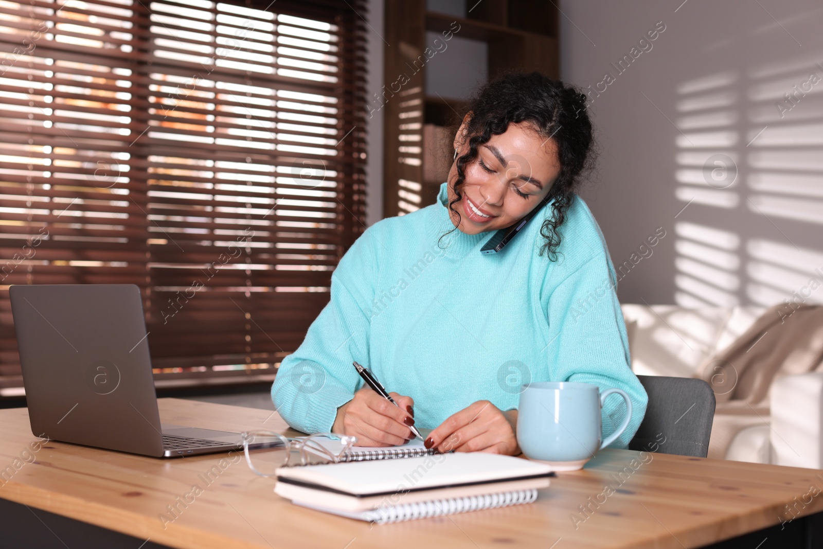 Photo of Beautiful woman talking on phone while working with laptop at desk in home office