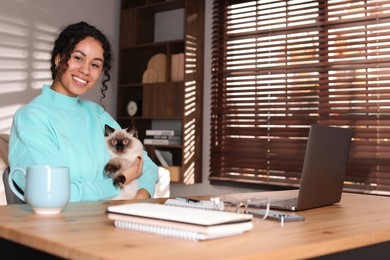 Photo of Beautiful woman with her cute cat working on laptop at desk in home office