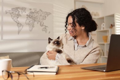 Photo of Beautiful woman with her cute cat working on laptop at desk in home office