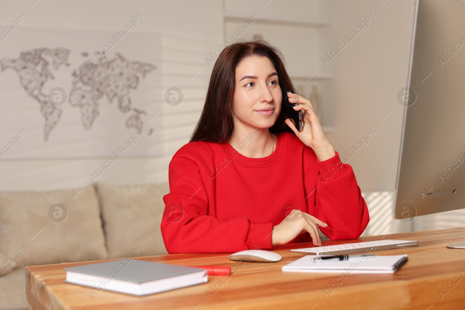 Photo of Woman talking on phone while working with computer at desk in home office