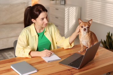 Photo of Young woman with her cute dog working on laptop at desk in home office