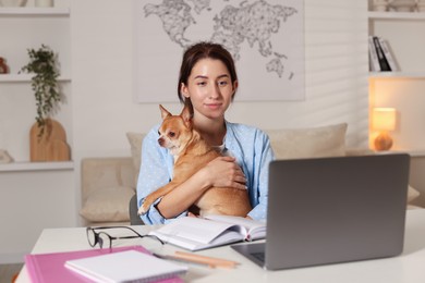 Photo of Young woman with her cute dog working on laptop at desk in home office