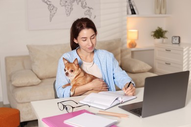 Photo of Young woman with her cute dog working on laptop at desk in home office