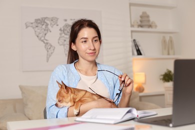 Photo of Young woman with her cute dog working on laptop at desk in home office