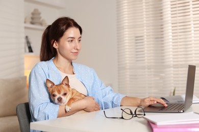 Photo of Young woman with her cute dog working on laptop at desk in home office. Space for text