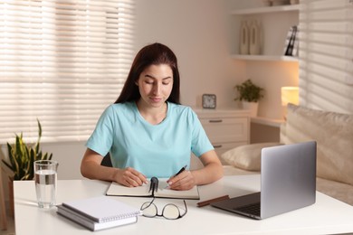 Photo of Young woman working on laptop at desk in home office