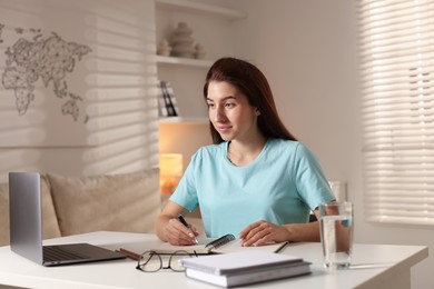 Photo of Young woman working on laptop at desk in home office