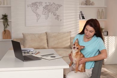 Young woman with her cute dog working on laptop at desk in home office. Space for text