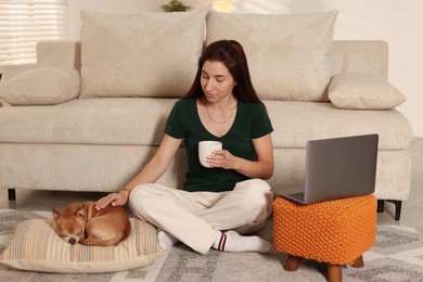 Photo of Young woman working on laptop while her cute dog sleeping beside at home