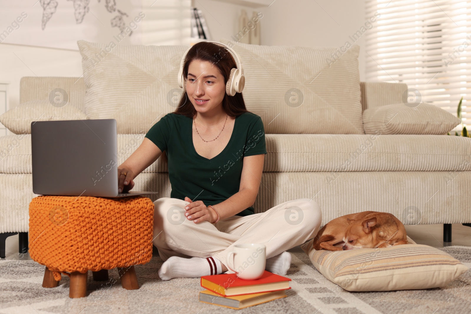 Photo of Young woman working on laptop while her cute dog sleeping beside at home