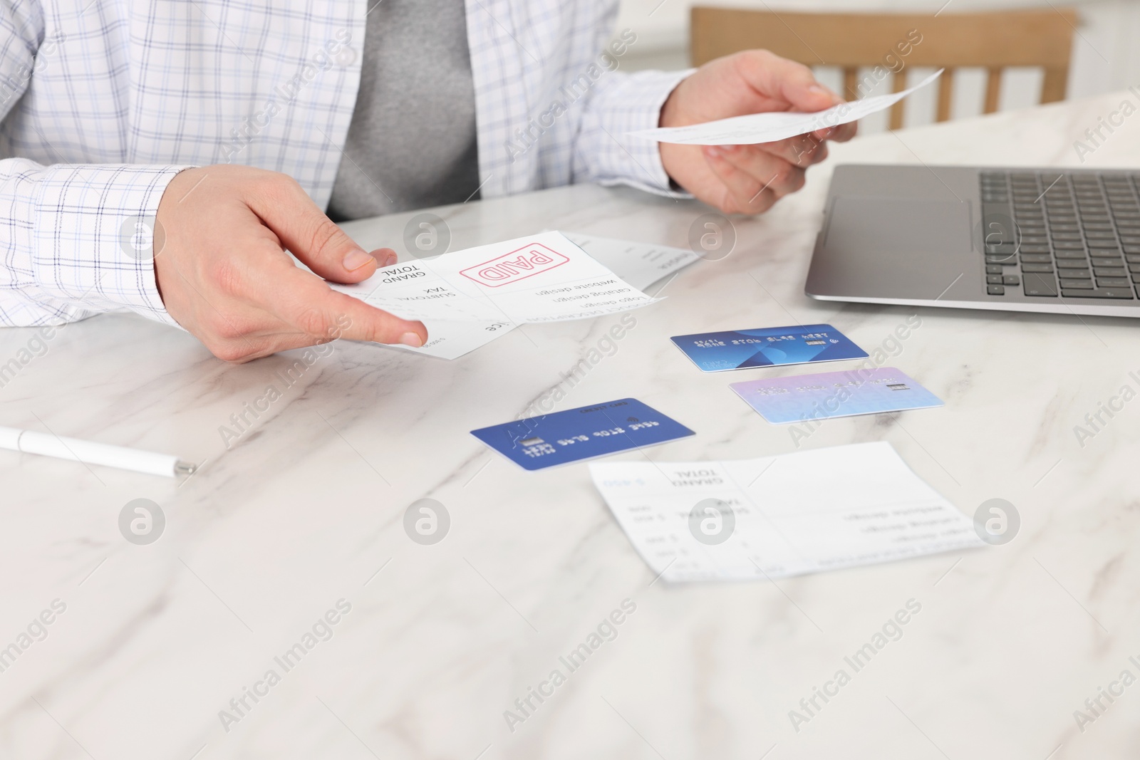 Photo of Paying bills. Man with reviewing invoices at white marble table indoors, closeup